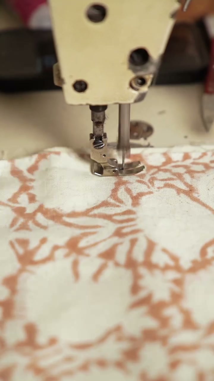 A close view of hands guiding printed fabric through a sewing machine